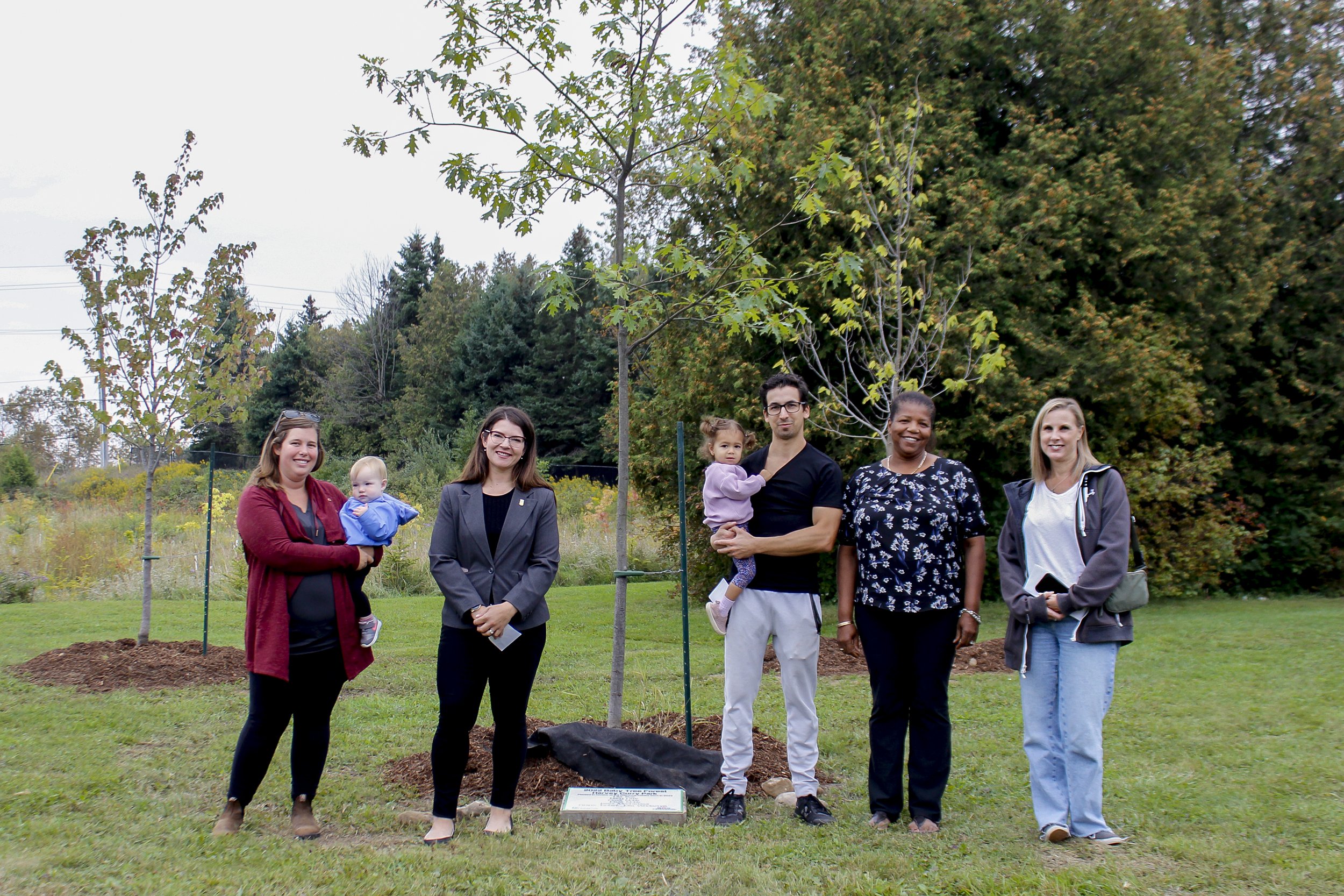 A group of people stand around the a new tree planted in honour of children born in 2022 as part of Sustainable Orangeville's Baby Tree Program.